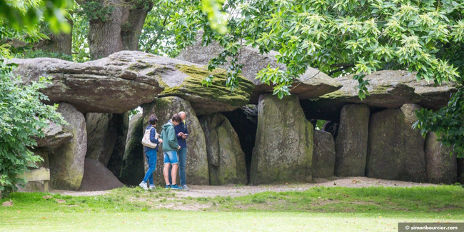 une famille regarde une carte d'énigmes au pied du tumulus de la Roche aux Fées